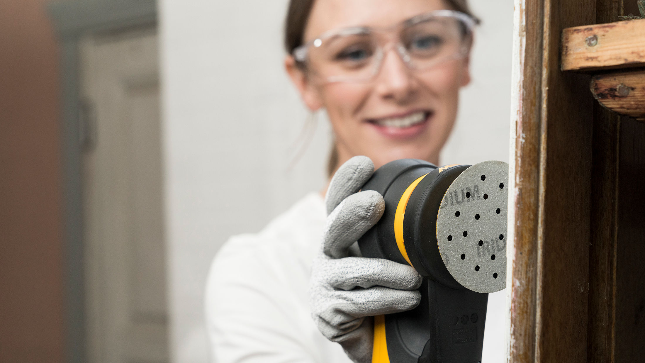 Een vrouw schuurt een houten paneel met een Mirka Deros 77mm 