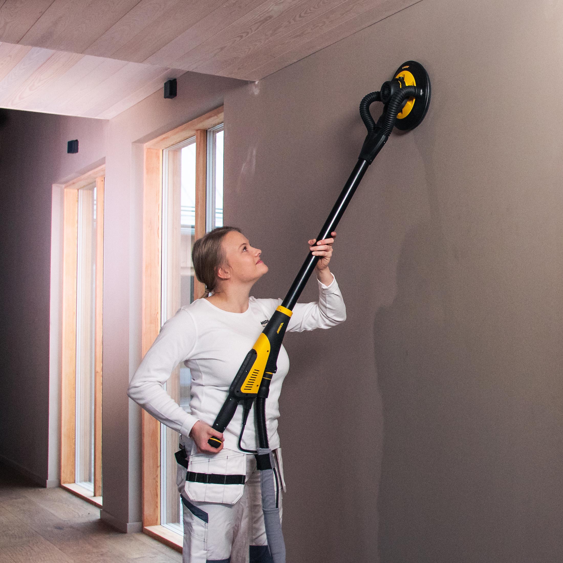 Jeune femme ponçant un mur beige avec une ponceuse mur et plafond Mirka Leros