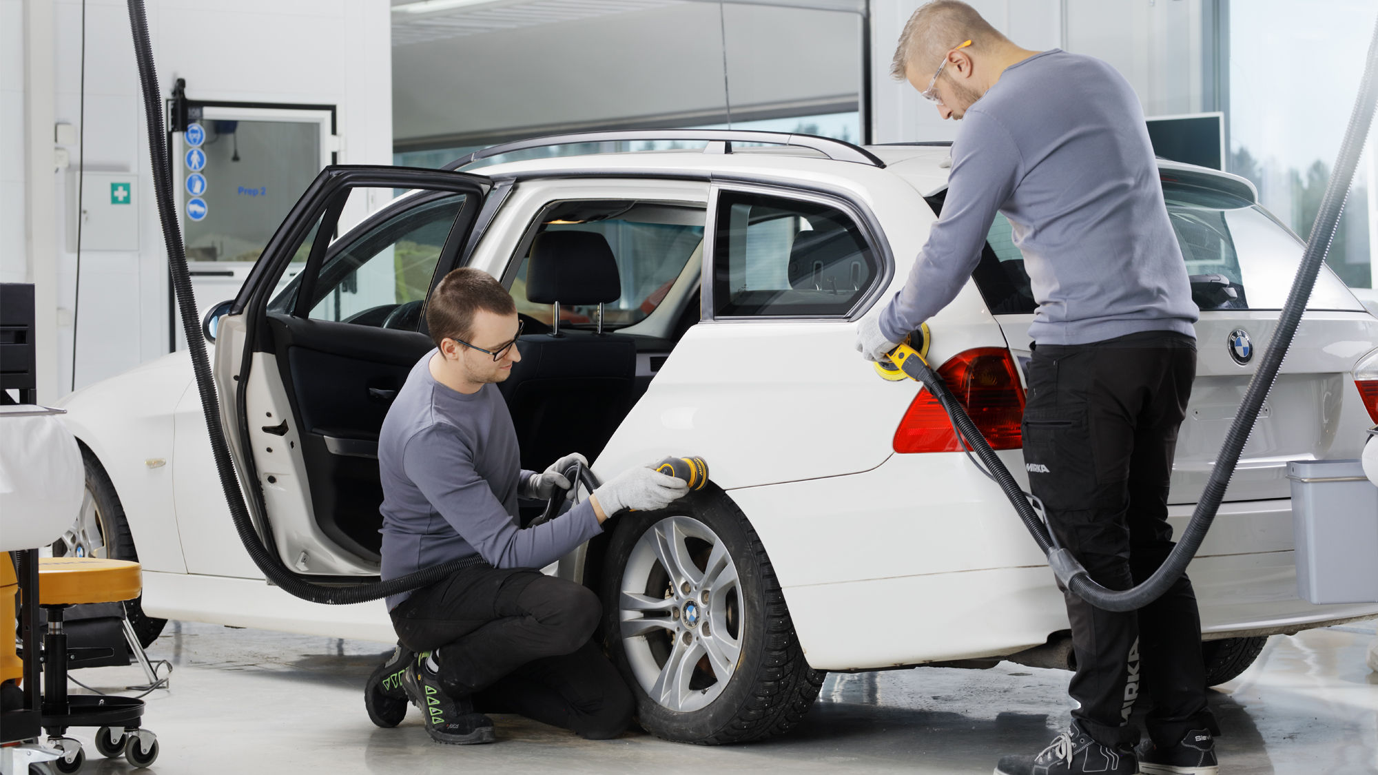 Two men sanding a car with Mirka sander tools.